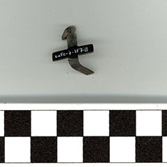 Photographie couleur d'une petite croix tordue en alliage cuivreux. Son code Borden y est visible.