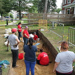 Colour photograph of the members of the archaeological team. Some are standing, while others are digging the ground.