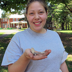 Colour photograph of a young trainee archaeologist holding a pipe in her hand.