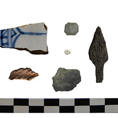 Colour photograph of six artifacts: French earthenware, an arrowhead, a bead, an Aboriginal pottery shard and two copper alloy wastes.